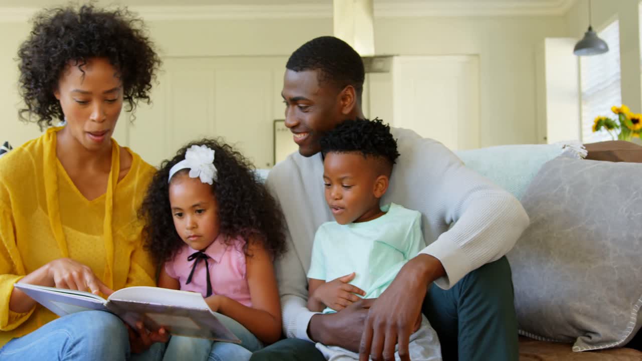 Vista frontale di una famiglia nera che legge un libro di storie in salotto 4k