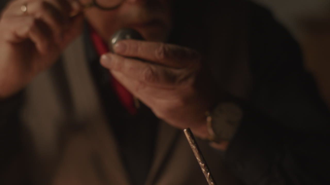 Older passionate man evaluates an old silver skull watch in his office at night