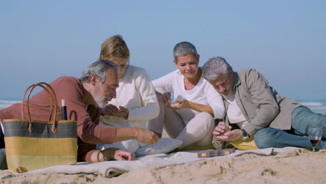 cheerful senior friends playing dominoes on seashore