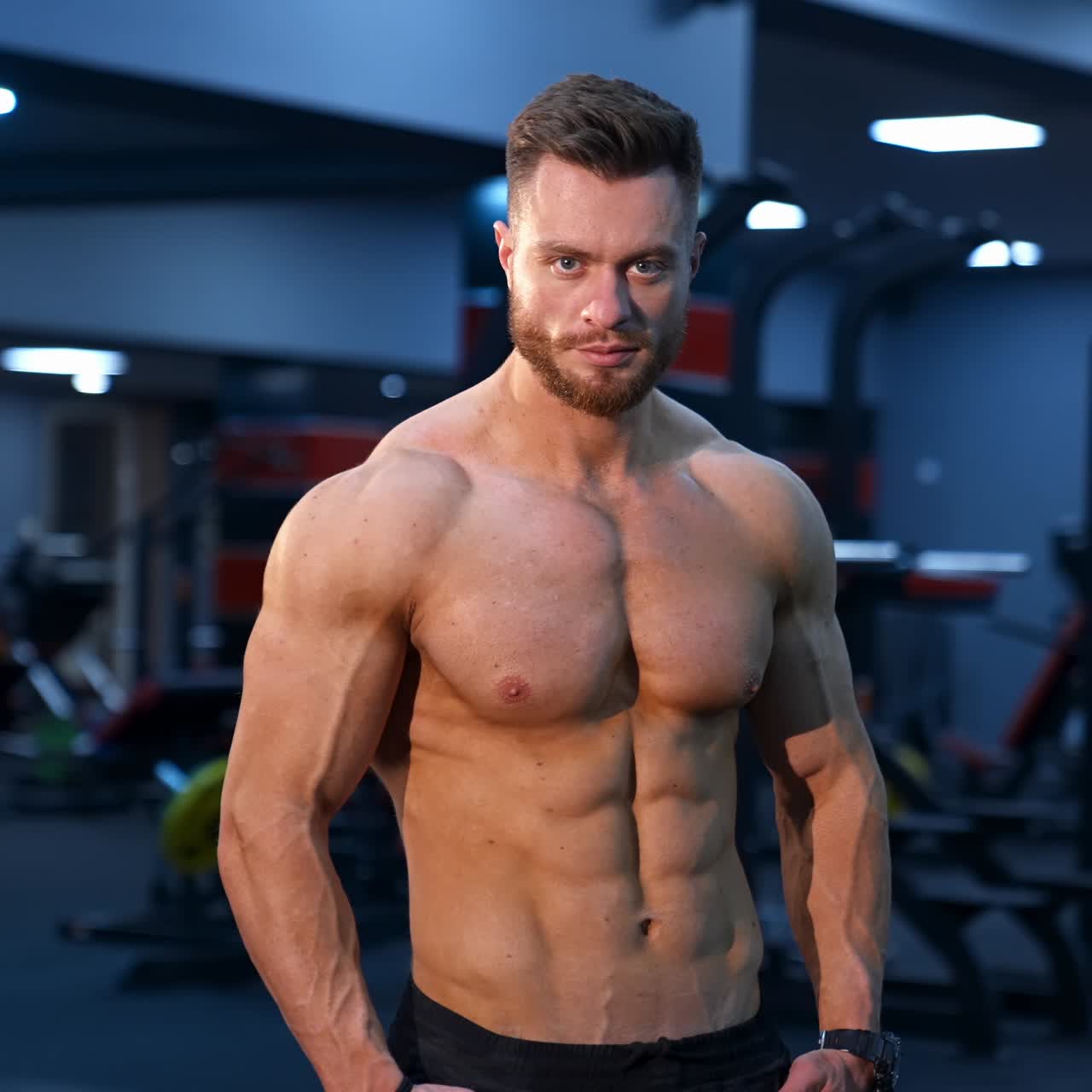 Muscle athlete strongman pumps muscules in a gym after heavy training. Perfect torso with strong abs. Handsome power male with naked torso