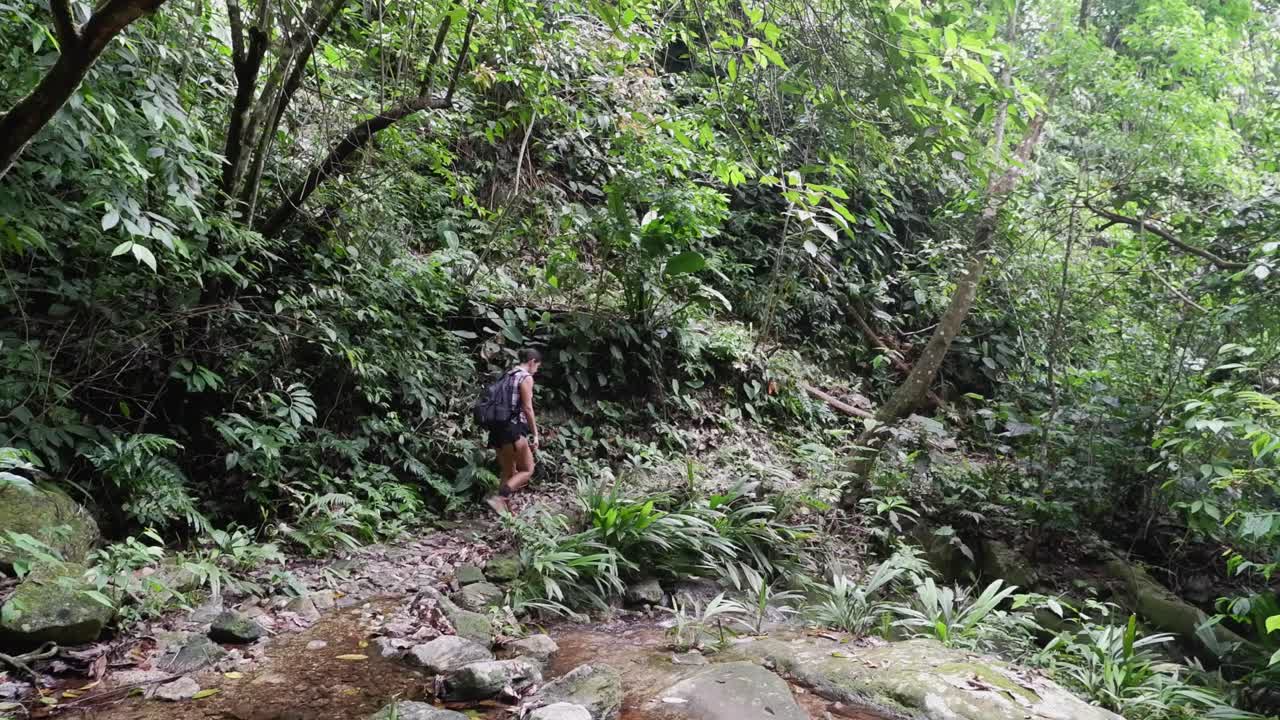 Mujer latina cruza un arroyo durante una caminata por la selva tropical en Honduras.