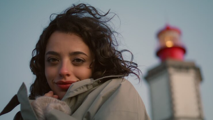 Ragazza sognante che si riposa in riva al mare con vista sul faro in primo piano. Donna felice e romantica che si riscalda.