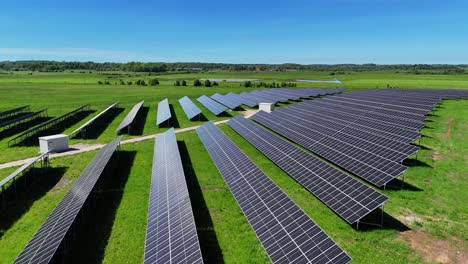 Un-Gran-Campo-De-Paneles-Solares-En-Un-Exuberante-Paisaje-Verde-Bajo-Un-Cielo-Azul-Claro,-Vista-Aérea