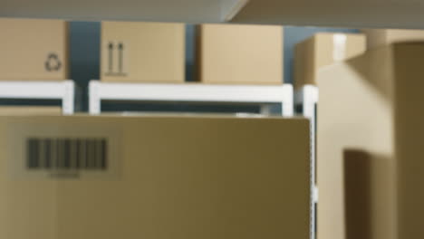 Close-Up-Of-Handsome-Postman-In-Glasses-Taking-Carton-Box-With-Bar-Code-From-Shelf-And-Smiling-In-Post-Office-Store