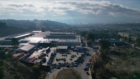 Industrial-park-near-Abrera,-Barcelona,-Spain-with-warehouses-and-parked-cars,-clear-day,-aerial-view