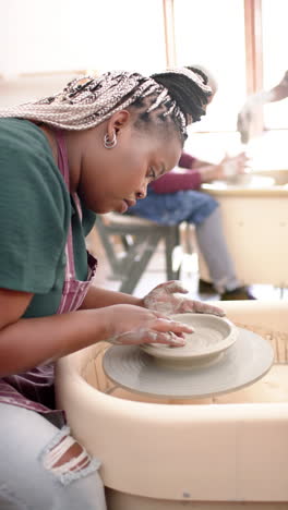 focused african american female potter using potter's wheel in pottery studio, slow motion