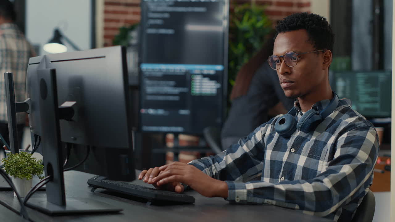 Portrait of focused programer writing code fixing glasses and smiling sitting at desk