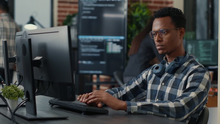 Portrait of focused programer writing code fixing glasses and smiling sitting at desk