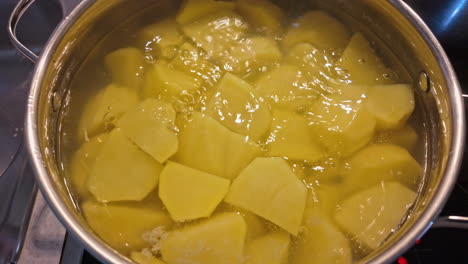 a silver pot simmers on the stove, filled with freshly cut potatoes boiling in water. the kitchen offers a warm atmosphere as the potatoes soften for a delicious meal.