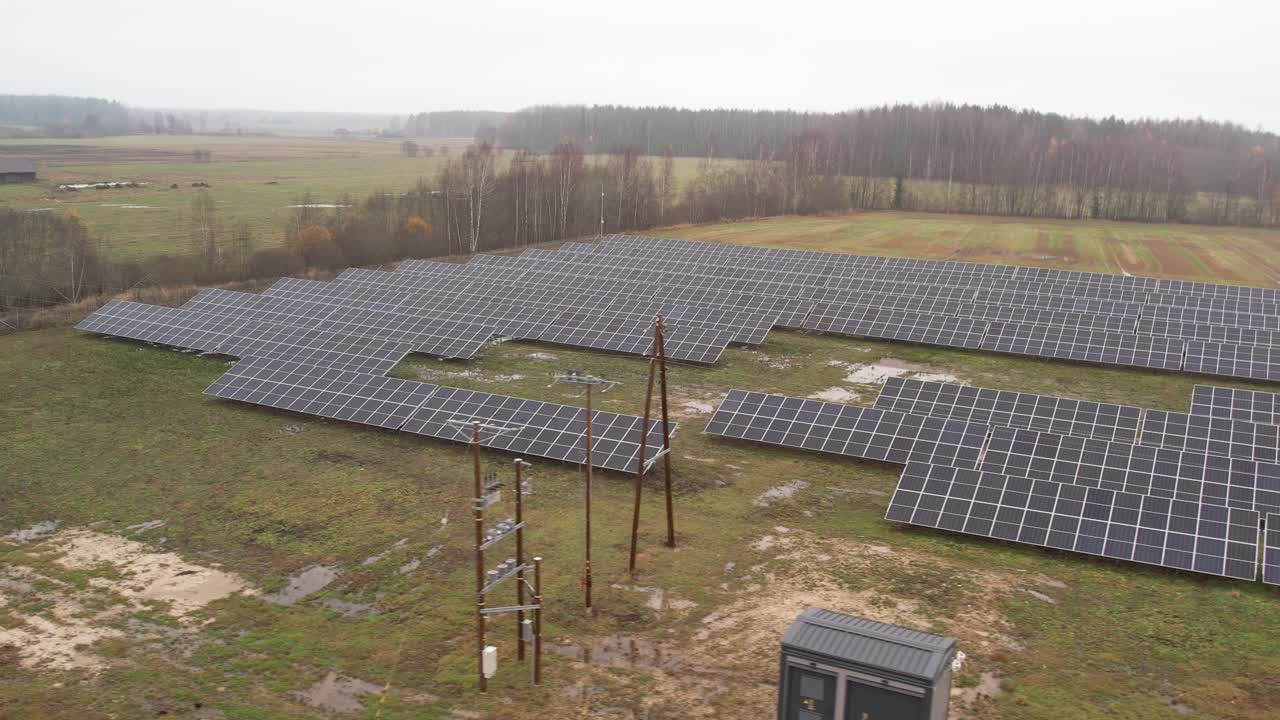 Rows of large solar panels aligned across a grassy field, viewed from above, capturing a renewable energy installation under overcast skies