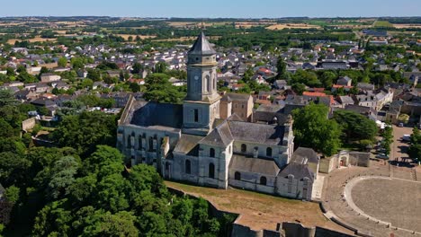 drone panning shot of saint-florent abbey church, showing the square, surrounding town, distant fields, horizon, and trees - france