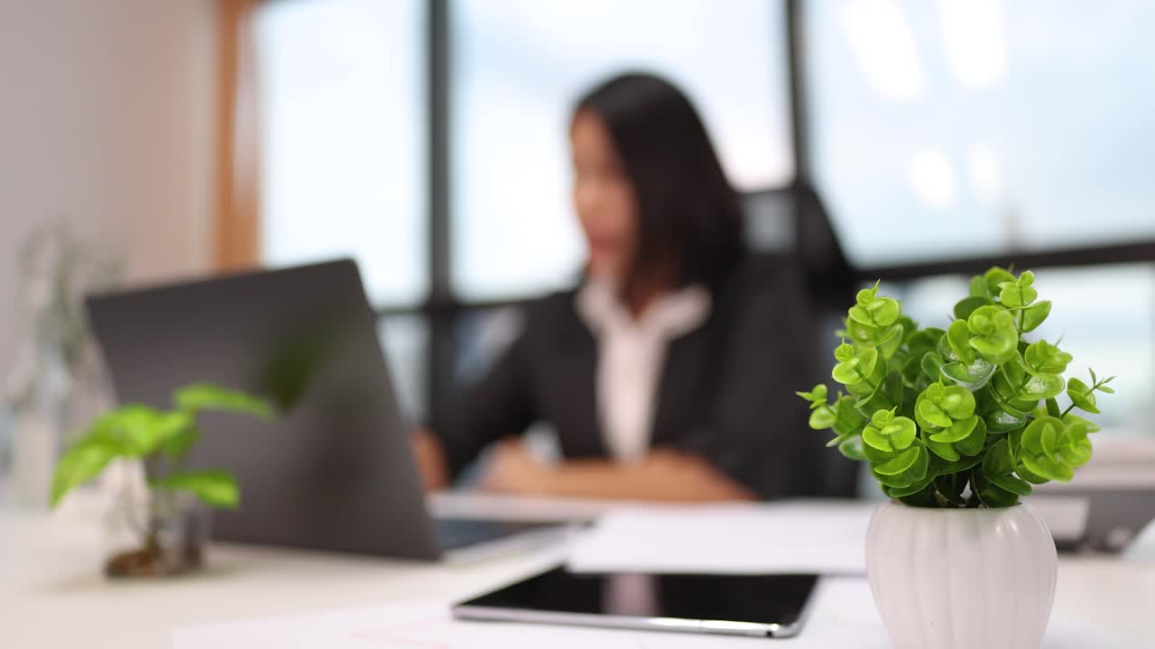 Imprenditrice concentrata che lavora al laptop in un ufficio moderno e luminoso con piante e sfondo sfocato