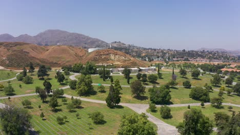 Super-wide-aerial-shot-flying-over-gravesites-towards-a-stone-mausoleum-at-a-mortuary-in-California