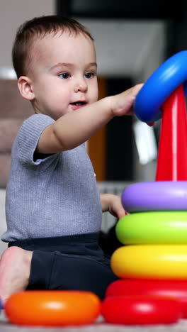 one year old boy constructing a toy pyramid. baby boy playing at home. living room backdrop. vertical video