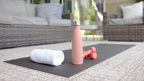 a yoga mat, white towel, pink water bottle, and dumbbells rest on patio