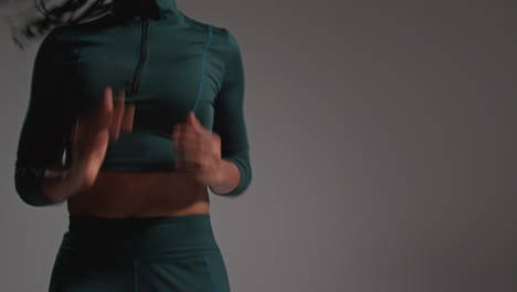 Close-Up-Low-Angle-Shot-Of-Female-Athlete-Wearing-Tracksuit-Training-In-Gym-Fitness-Class-Running-On-The-Spot-Against-Plain-Background