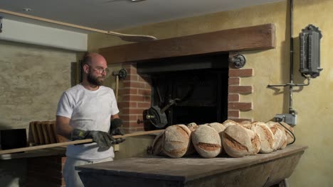 large shot in the bakery, baker’s peel going out with some crusty and goldy loaf bread, storing them to rest on a rustic wooden table