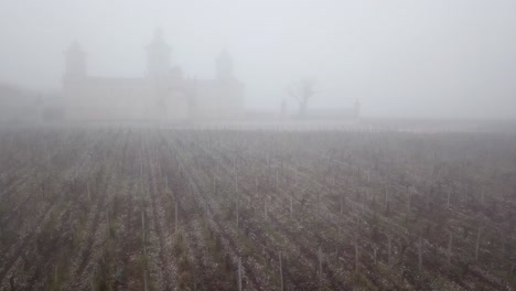 Adelante-Aéreo-Ascendiendo-Sobre-El-Viñedo-Con-El-Castillo-De-Cos-D&#39;estournel-En-Segundo-Plano-En-Un-Día-Brumoso,-Burdeos-En-Francia