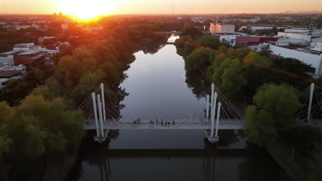 Perspectiva-De-Pájaro-Sobre-La-Puesta-De-Sol-Sobre-Un-Río-Con-Panorama-De-Paisaje-Urbano-Y-Puente-Peatonal