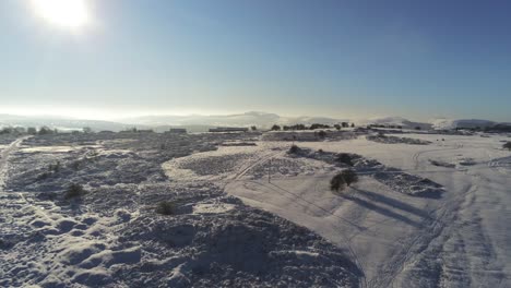 Snow-covered-rural-winter-countryside-track-footprint-shadows-terrain-aerial-view-pan-slow-right-rising