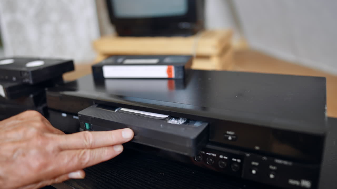 Hand takes a tape from the VHS recorder and puts into the player. Man pushes the button on the panel of the device. Close up