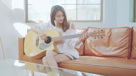 young cute girl sitting cross-legged on the sofa enjoyed playing guitar