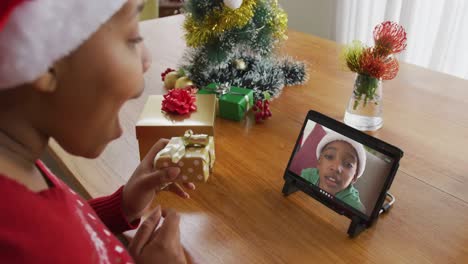 Mujer-Afroamericana-Con-Sombrero-De-Santa-Usando-Tableta-Para-Videollamada-Navideña-Con-Niño-En-Pantalla