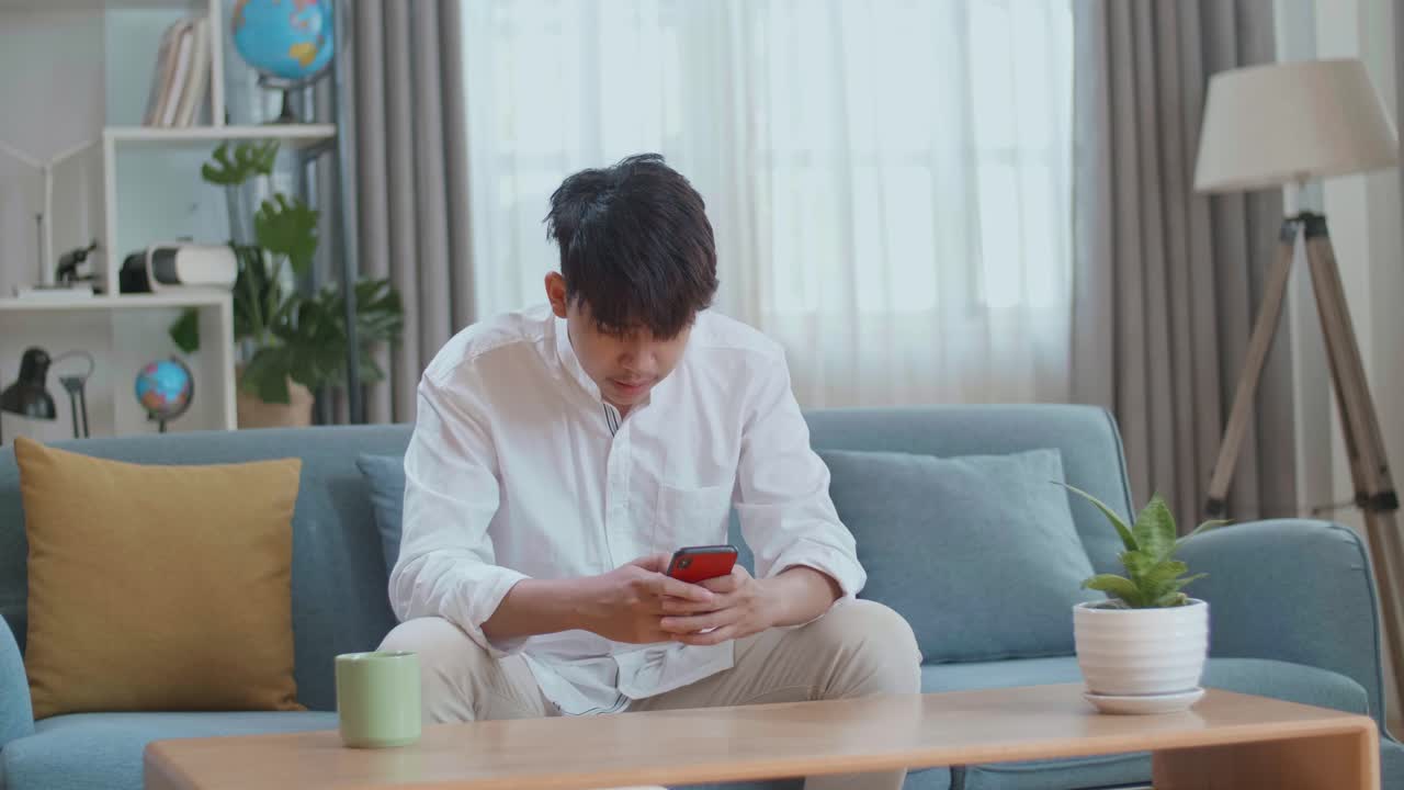 Asian Man Being Tired While Using Smartphone In The Living Room