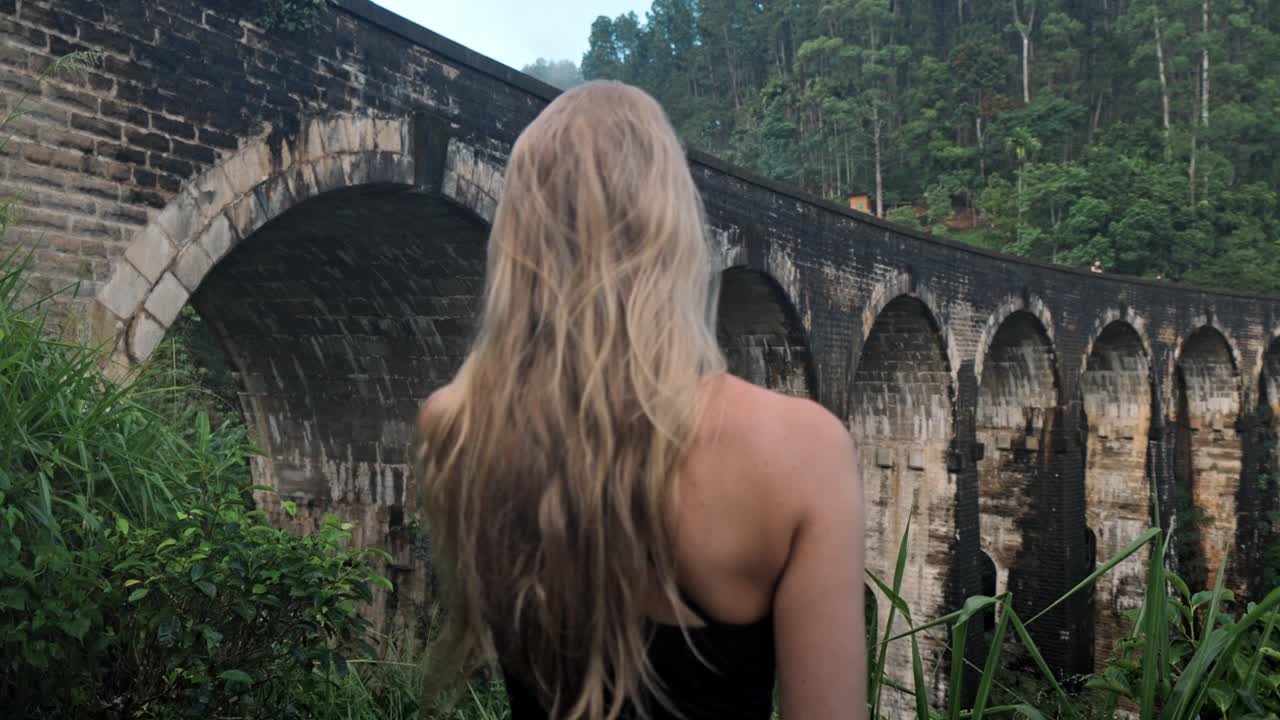 A young woman observes the historic Nine Arch Bridge from a nearby hillside in Ella, Sri Lanka.