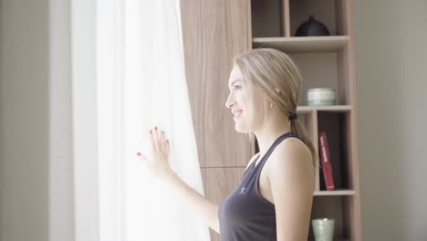 lady looks outside window with bright sun and smiles happily at view