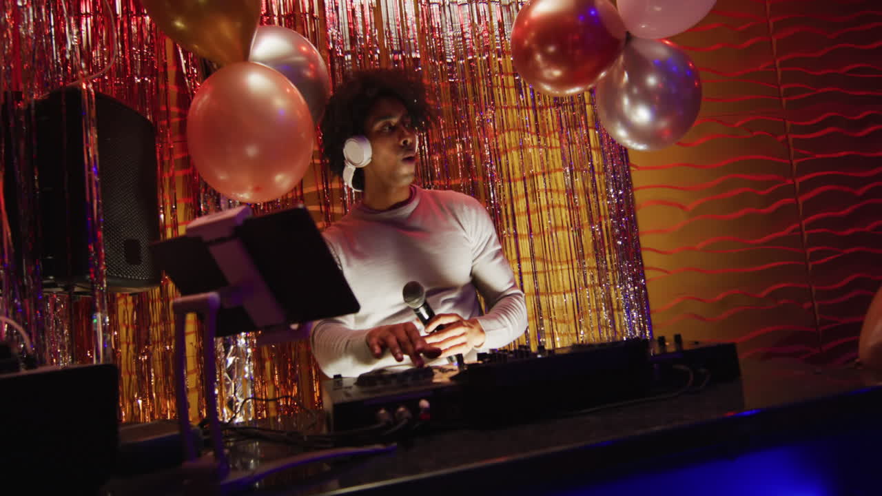 Video of happy african american male dj playing music, dancing and using microphone at a nightclub