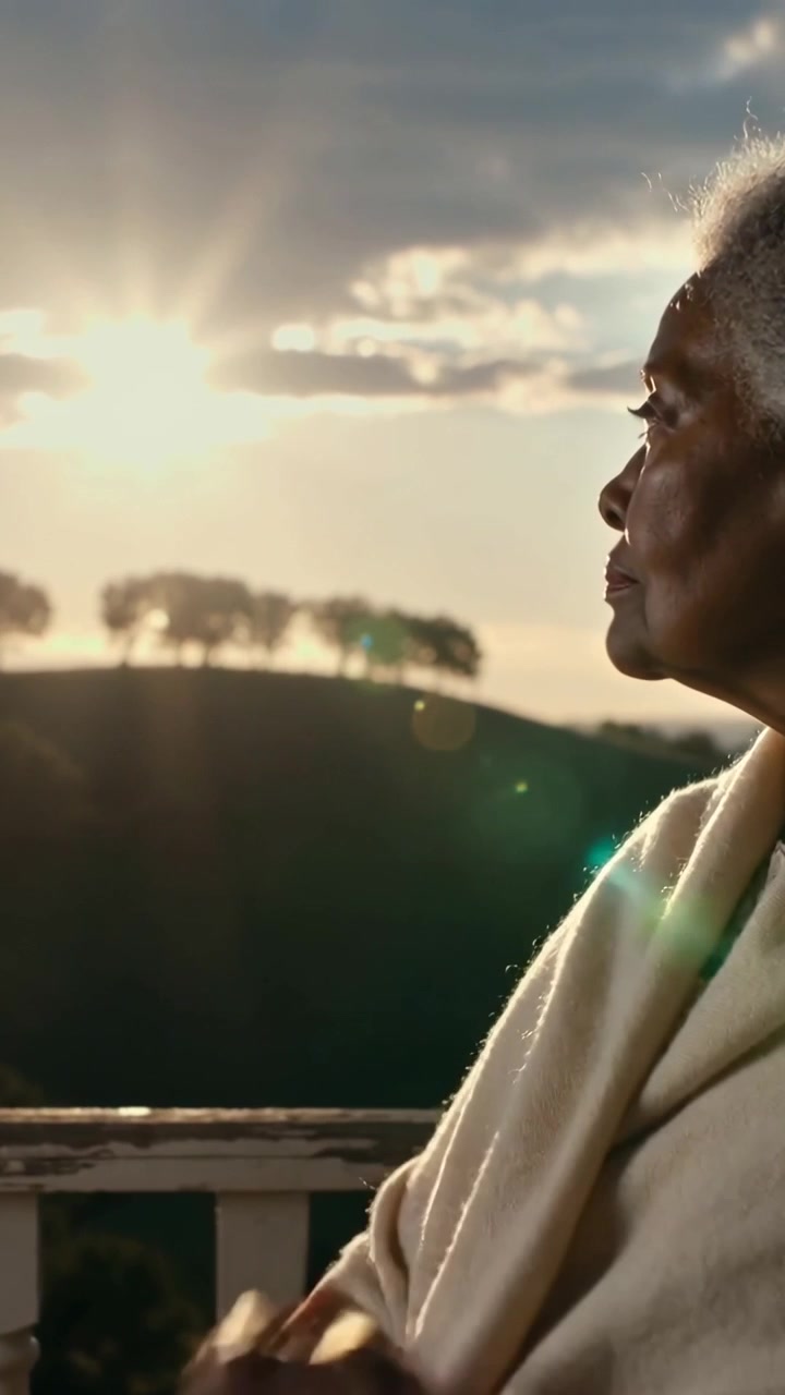 Video verticale: Sole che tramonta, una donna anziana si avvolge in uno scialle sul portico mentre guarda il tramonto, spazio per il testo.