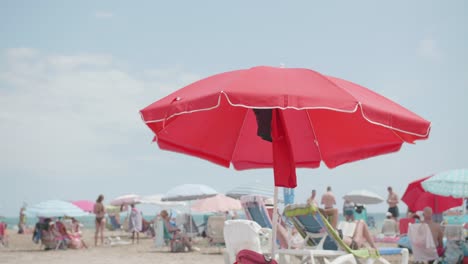 red beach umbrella and chairs on the white sand - tropical beach with tourists during summer - static shot