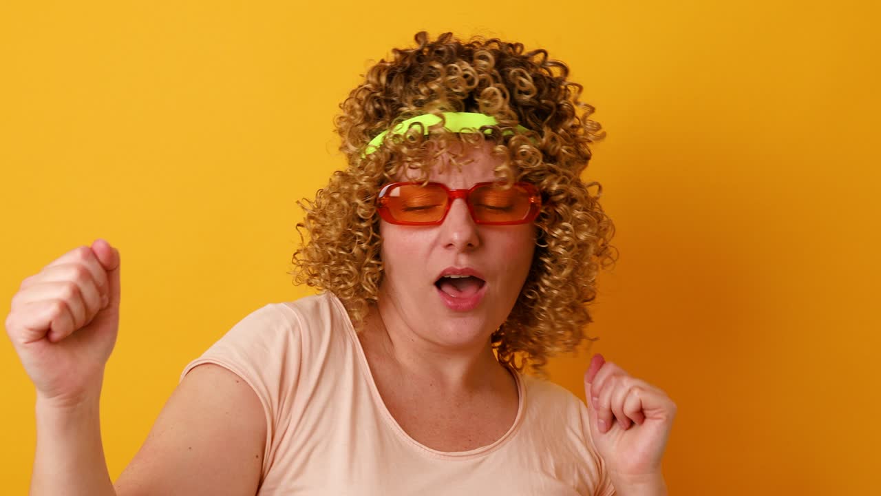 video de una mujer joven y bonita de 30 años levanta los brazos y baila a su música favorita, olvidando todos los problemas aislados sobre un fondo amarillo