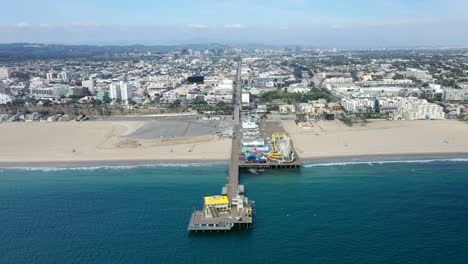 Aguas-Turquesas-De-La-Playa-Que-Recorren-El-Muelle-De-Pesca-Y-El-Parque-De-Diversiones-De-Santa-Mónica-En-California,-Nosotros-Con-Una-Amplia-Vista-Del-Paisaje-Urbano