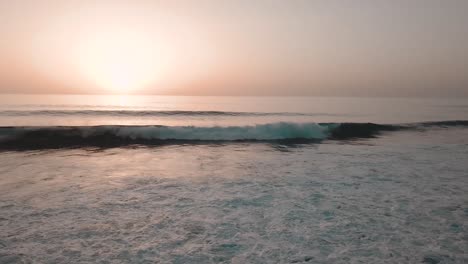 Slow-panning-shot-of-orange-glowing-sunset-over-sea-with-small-breaking-waves-on-rocky-shore-in-foreground