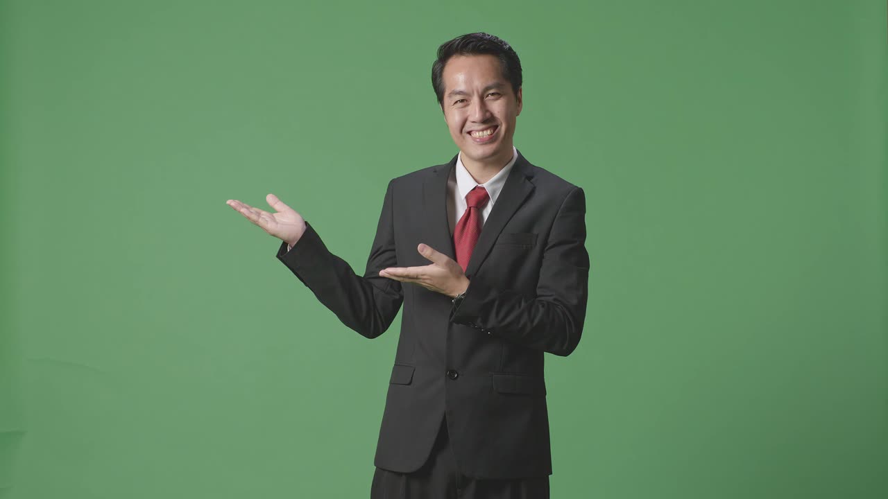 緑色のスクリーンに立っている間開いた手の掌を示すアジアのビジネスマン