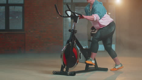 Mujer-Atlética-Montando-Una-Rutina-De-Entrenamiento-En-Bicicleta-Estacionaria-Giratoria-En-Un-Gimnasio-De-Niebla,-Pérdida-De-Peso-En-Interiores