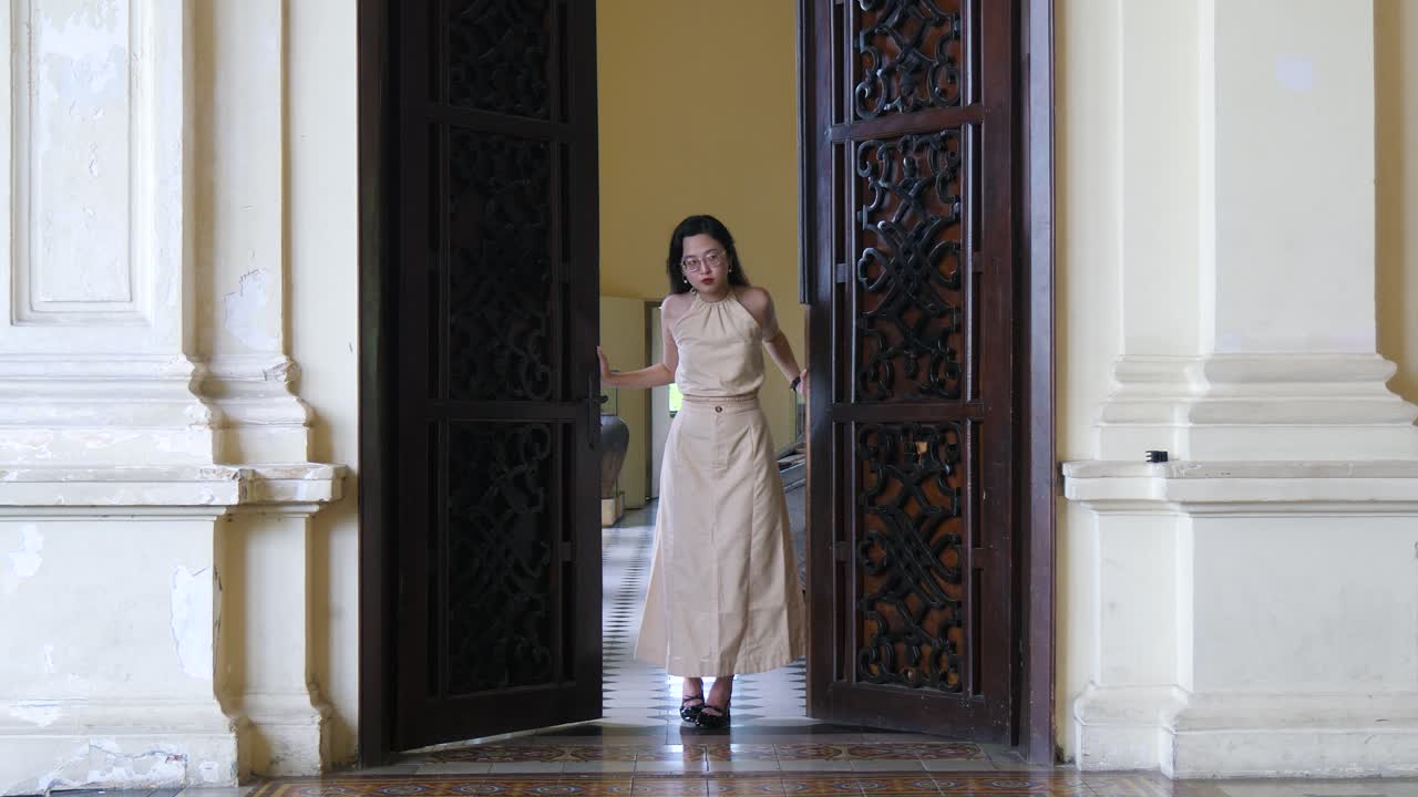 mujer en vestido beige camina a través de puertas de madera ornamentadas en un edificio histórico