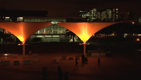 gente caminando en el centro de la ciudad de lisboa, a altas horas de la noche, farolas de color naranja, siluetas negras de personas caminando cerca de la entrada del oceanario de lisboa