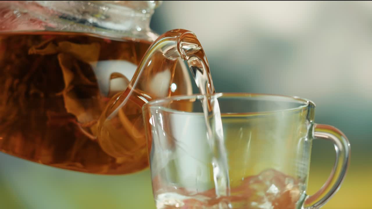 Close-up of Tea Being Poured from a Glass Teapot into a Cup