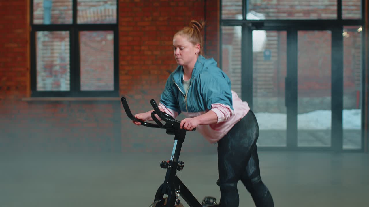 Athletic woman riding on spinning stationary bike training routine in haze gym weight loss indoors