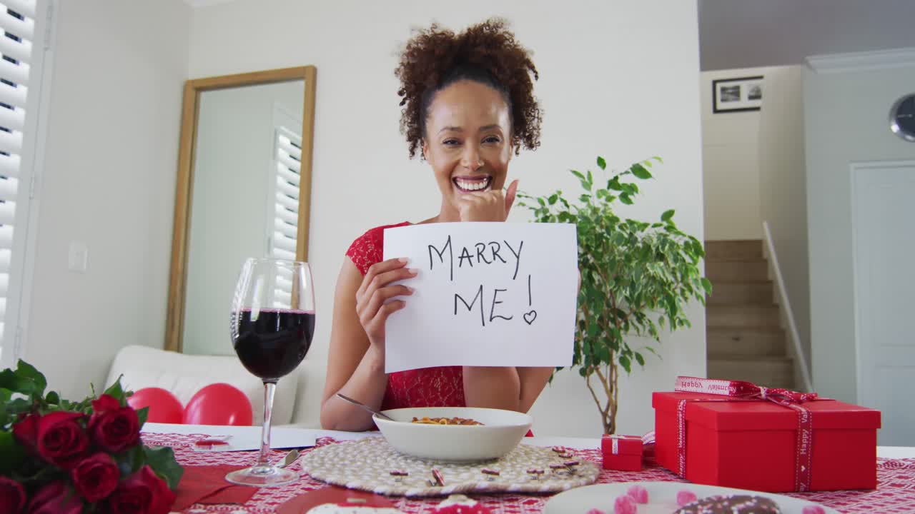 Donna di etnia mista in videochiamata per un appuntamento di San Valentino, che tiene in mano un cartello di proposta di matrimonio.