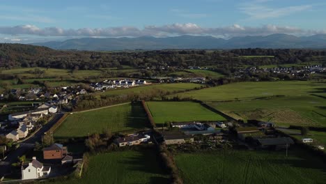 Aerial-view-orbiting-over-small-town-Welsh-community-farmland-countryside-with-Snowdonia-mountain-range-on-the-horizon