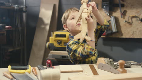 cute caucasian boy playing with wooden plane toy in carpentry workshop