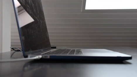 Side-view-of-a-laptop-on-a-desk-with-the-keyboard-and-a-white-cable-plugged-in-to-charge