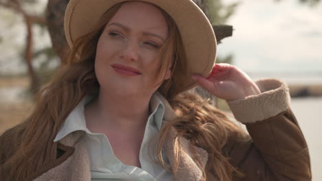 portrait of a curvy smily red haired woman wearing a camel hat in the forest