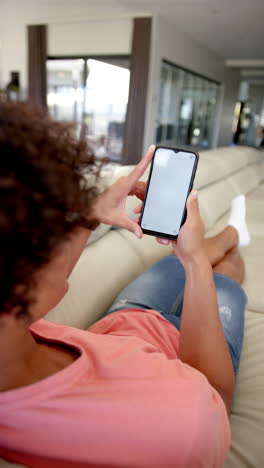vertical video: young biracial male homeowner sitting on couch, holding smartphone