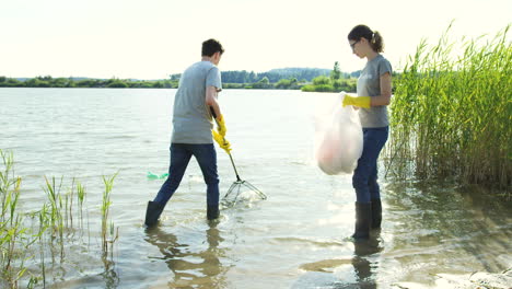 Ein-Paar-Freiwillige-Sammeln-Müll-Vom-Seegrund-Und-Sammeln-Ihn-In-Der-Plastiktüte,-Während-Sie-Den-See-Reinigen