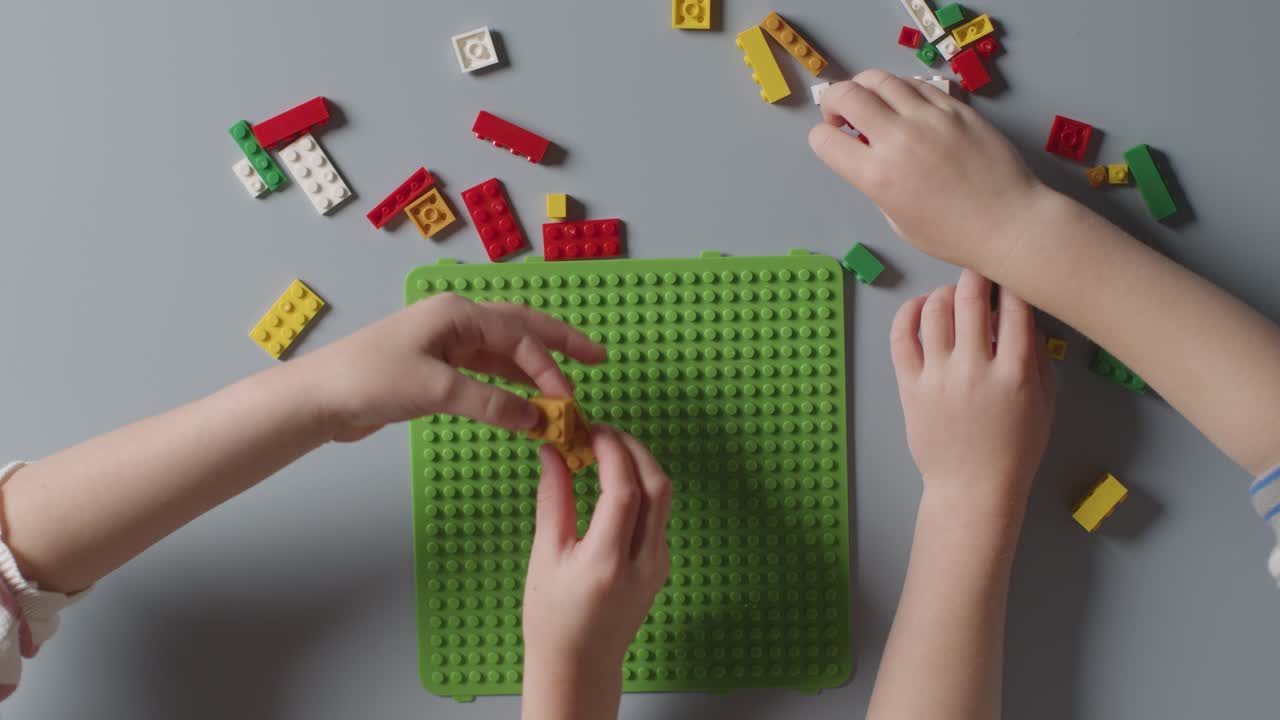 회색 배경에 플라스틱 건설 벽돌로 놀고 있는 두 아이의 오버헤드  ⁇